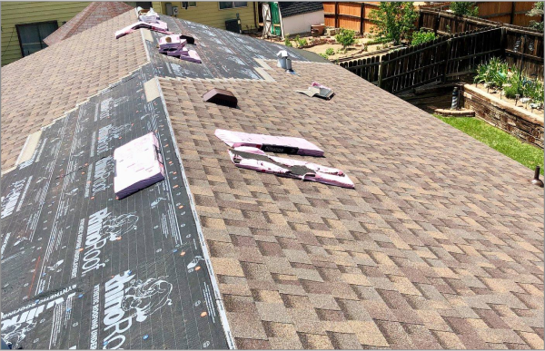 Residential roof with brown shingles being repaired, showing black underlayment and tools scattered across surface