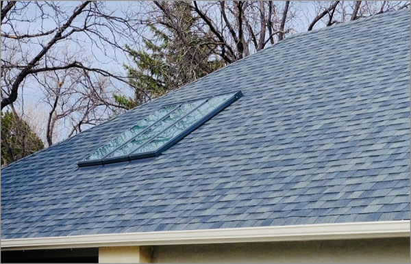 Solar panels installed on gray shingled residential roof with bare trees in background