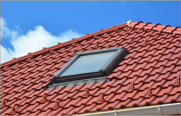 Red clay tile roof with modern skylight window against blue sky with clouds