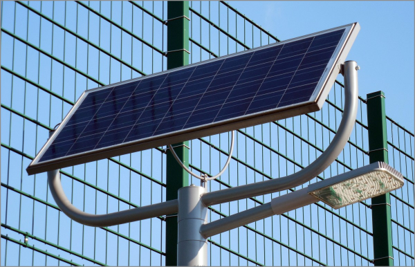 Solar panel mounted on metal pole with LED street light against chain link fence