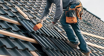 Roofer installing dark gray tiles on residential roof with tools and safety gear