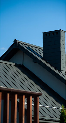 Modern house with dark metal roof and brick chimney against clear blue sky