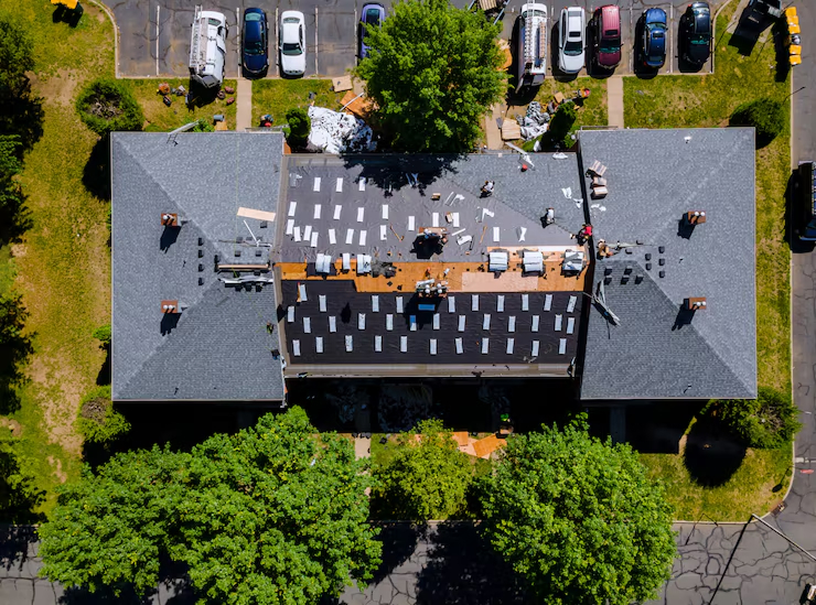 Aerial view of roof repair work in progress with workers, materials, and equipment scattered across a gray shingled rooftop