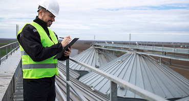 Construction worker in safety vest and hard hat inspecting metal roof structure