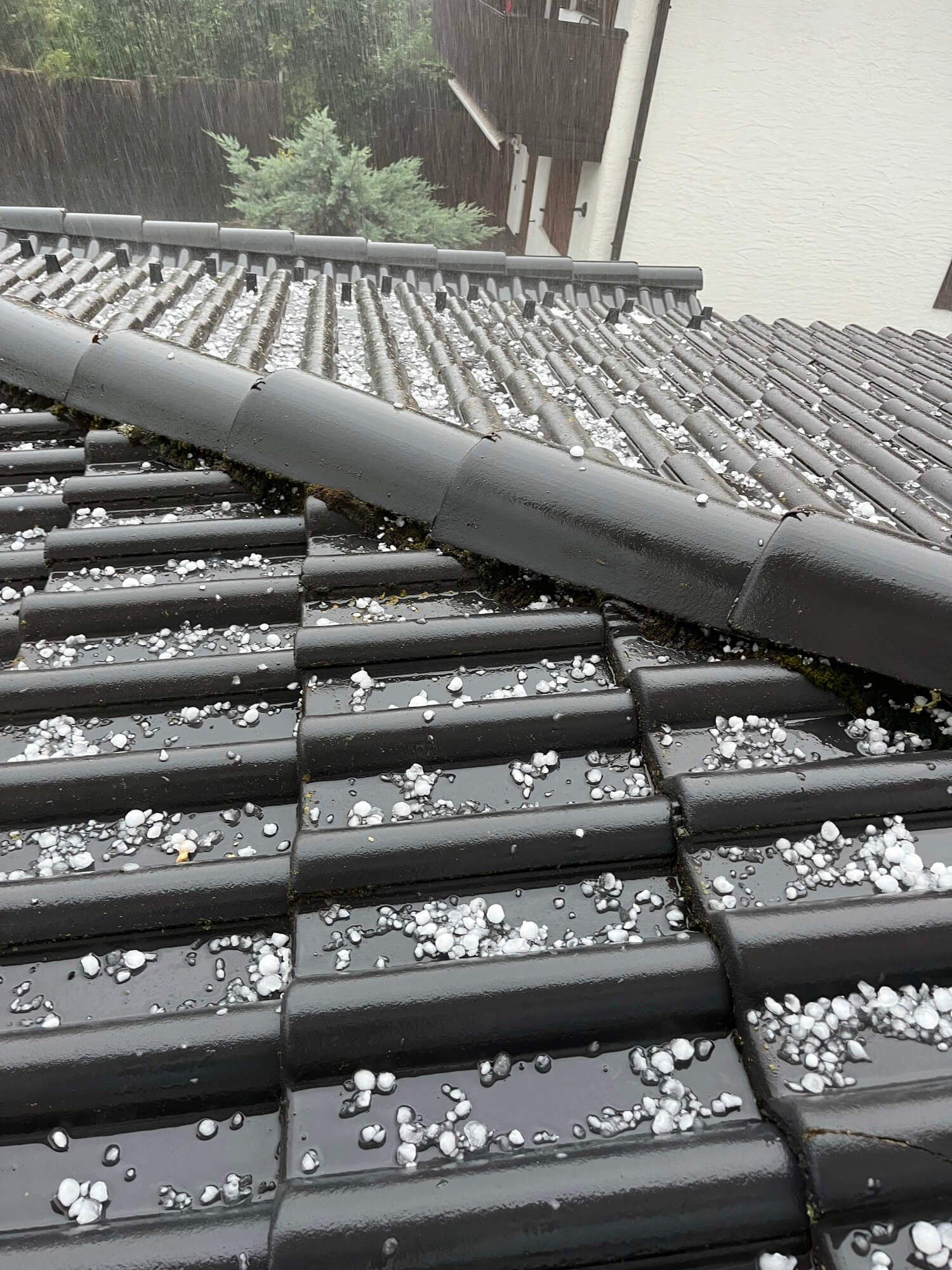 Severe hail damage on gray roof tiles with large white hailstones scattered across surface
