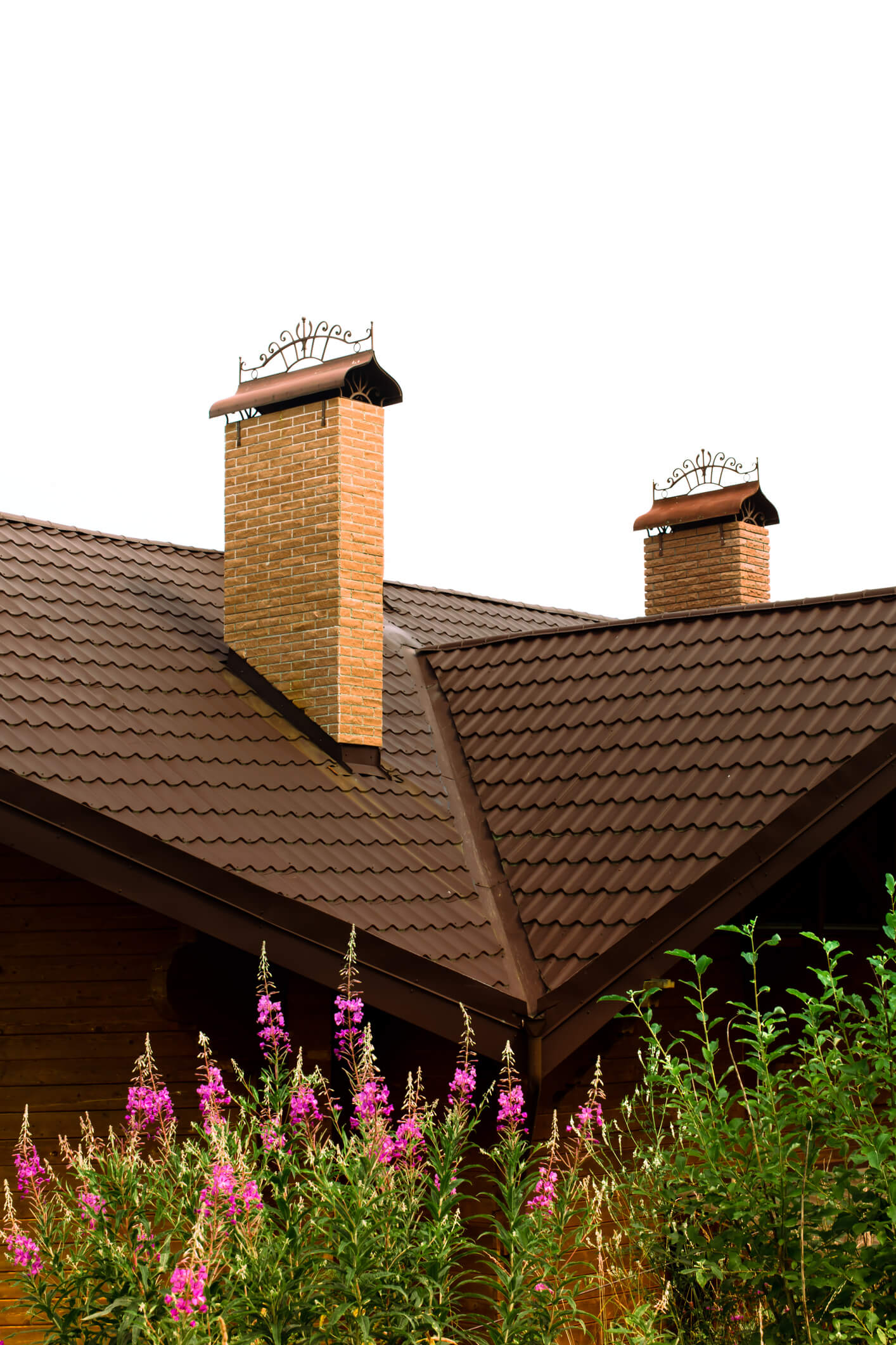 Brown tile roof with two brick chimneys and decorative metal caps above garden