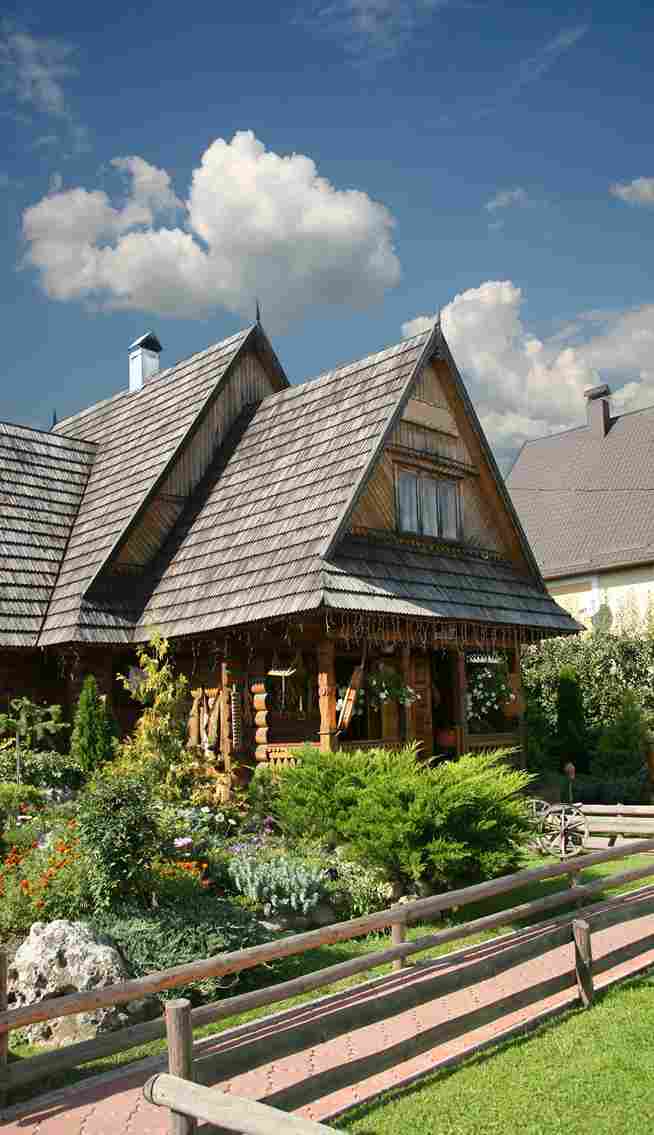 Traditional wooden house with steep roof and lush garden under blue sky with clouds